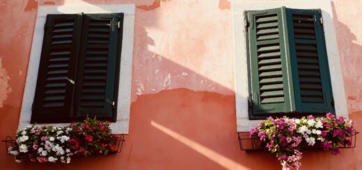 Hauswand mit geschlossenen Fensterläden, darunter Blumenkästen