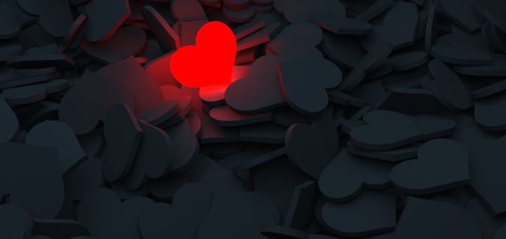 Inmitten von schwarzen Herzen leuchtet ein einzelnes rotes Herz